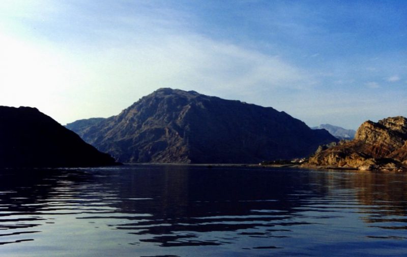 Wide stretch of blue water with a rocky mountain (no snow) in the background.