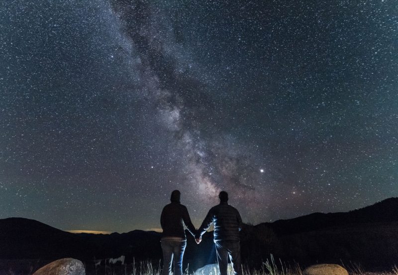 A couple holding hands under the Milky Way, with bright Jupiter shining to one side.