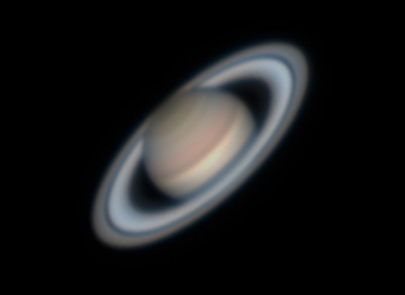 A slightly fuzzy telescopic view of colorful, striped Saturn and its rings.