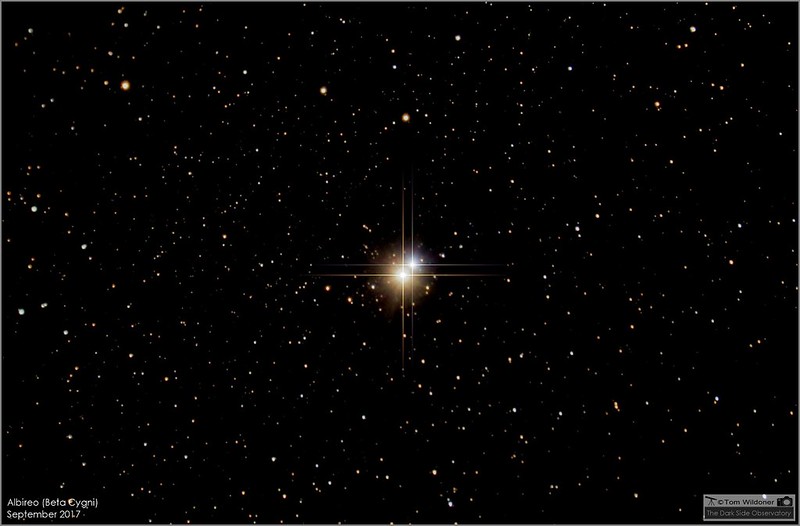A star-studded field of mostly faint stars with two bright stars in the center, an orange-yellow and a dimmer blue.