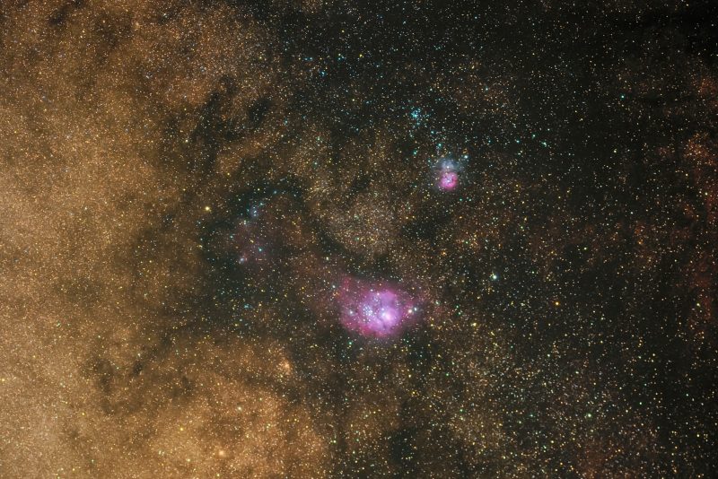 Un câmp stelar foarte dens, cu un punct roz lângă partea de jos și dreapta sus, în albastru și roz.