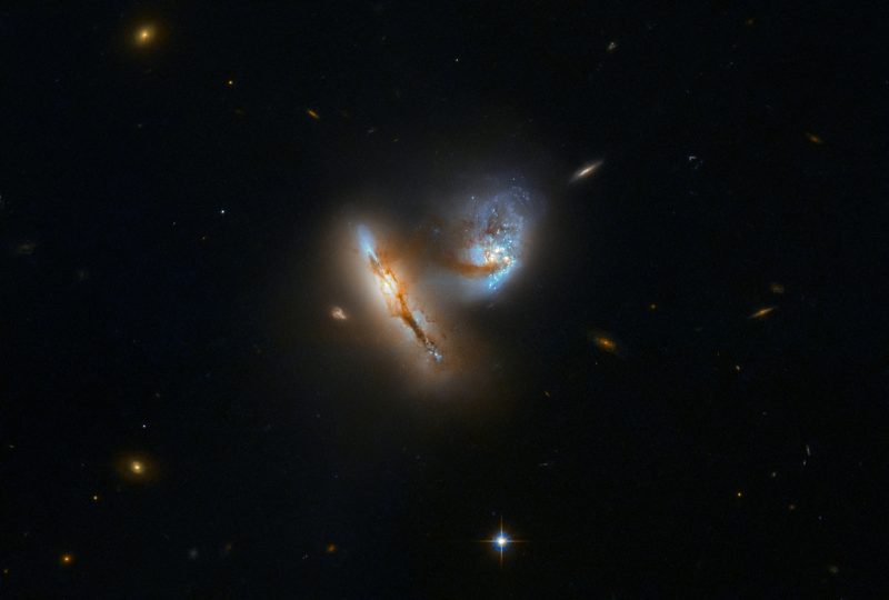 2 glowing oblong galaxies, one edge-on & the other face-on, barely touching, with black background.
