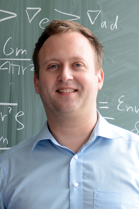 Smiling professor in front of blackboard.