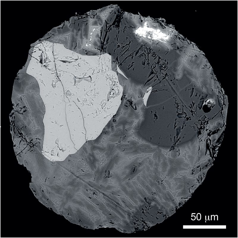 Microscopic view of a cross-section of a micrometeorite with dark and light gray patches.