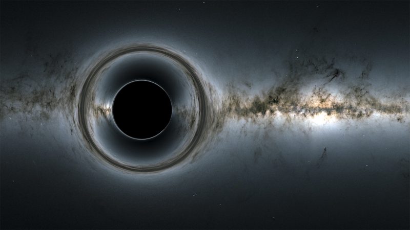Black circle with brighter rings around it and galaxy in background.
