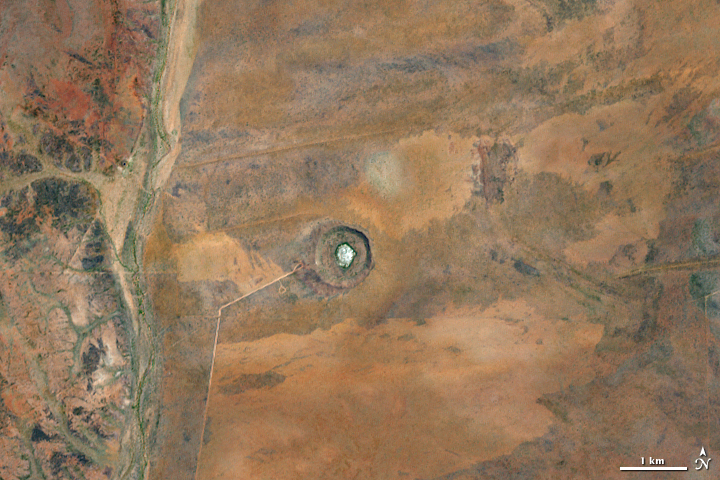 A tiny white circle surrounded by a brown rim in a vast area of dark tan desert.