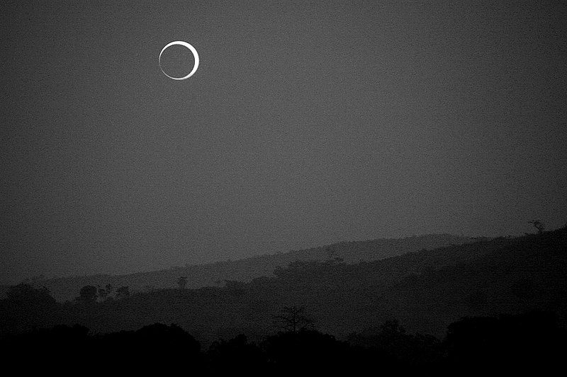Annular eclipse beautifying early morning sky over shadowed landsca;e.