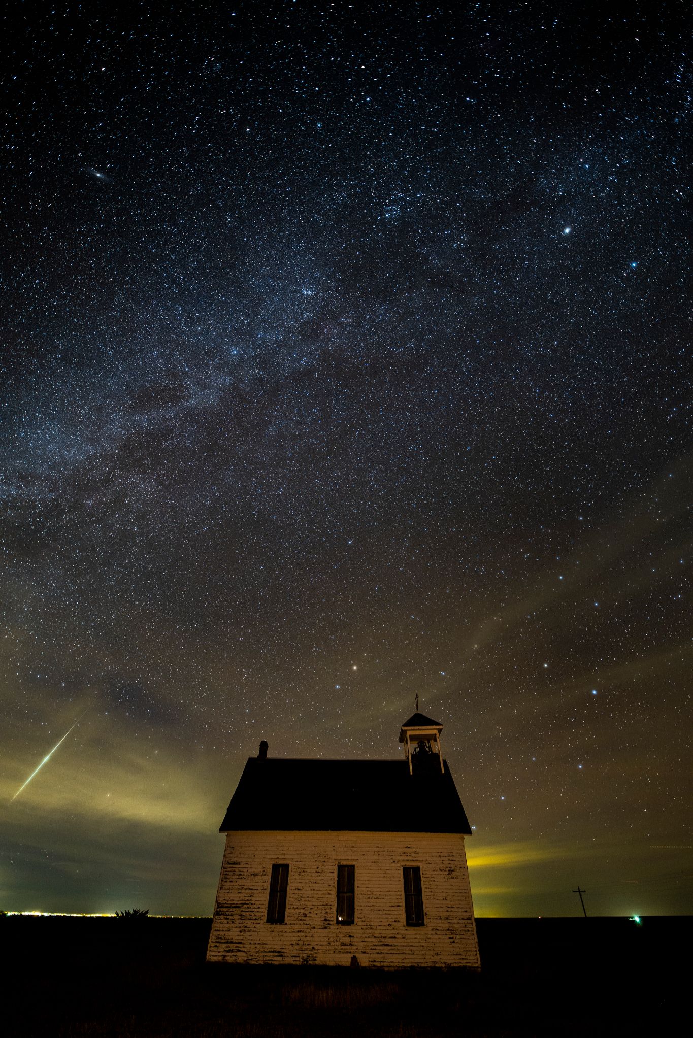 Small, old church in isolated location, dark sky, with a bright meteor streaking through the scene.