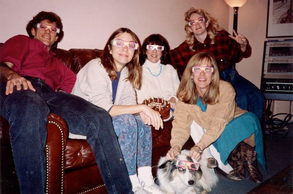 Five people and a dog, with big funny glasses on, lounging on a couch.
