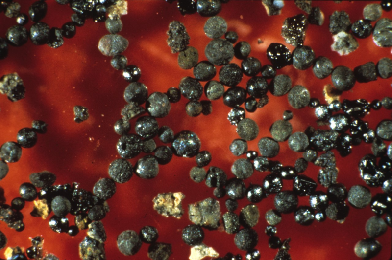 Many tiny, dark metallic spheres on red background.
