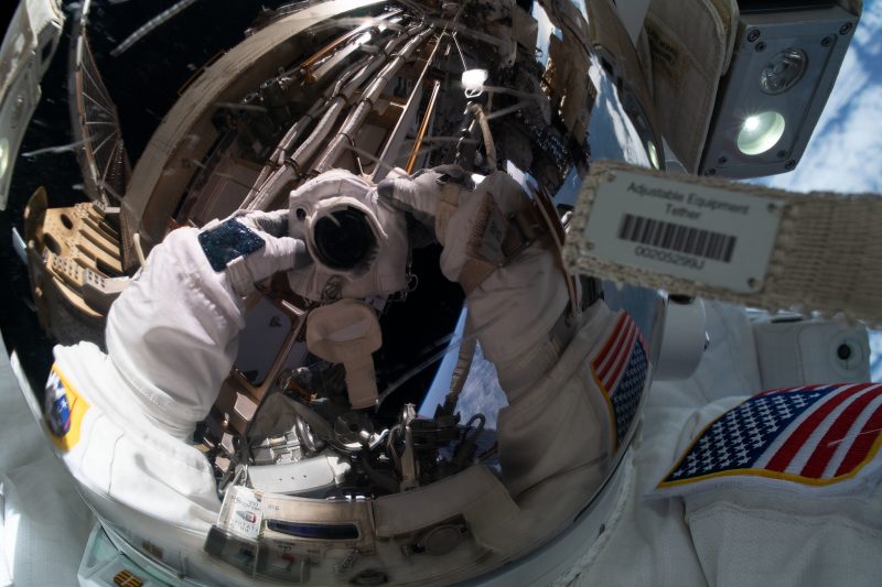 Reflection of camera in shiny, spherical visor of helmet of astronaut.