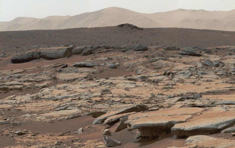 Rocky and sandy terrain with mountains in background.