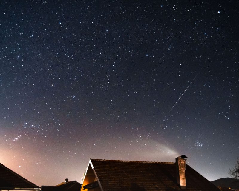 A bright meteor streak past the roof of a house.