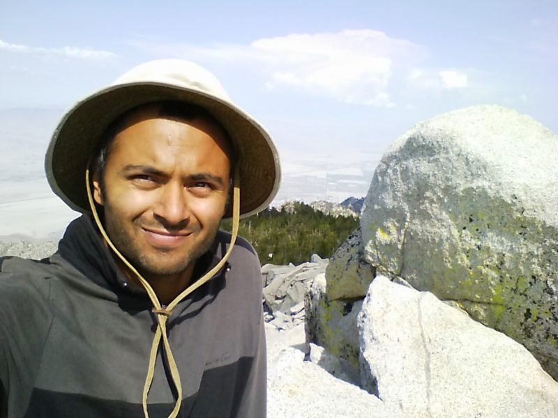 Smiling man in a hat with a rock behind him.