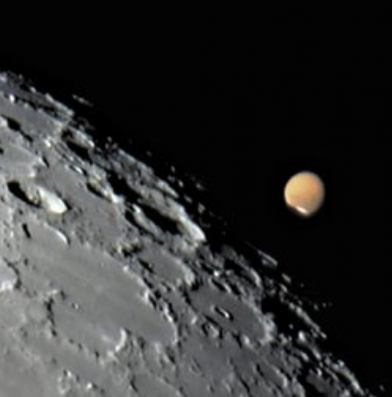 A telescopic view of the moon's cratered limb, with the red disk of Mars disappearing behind it.