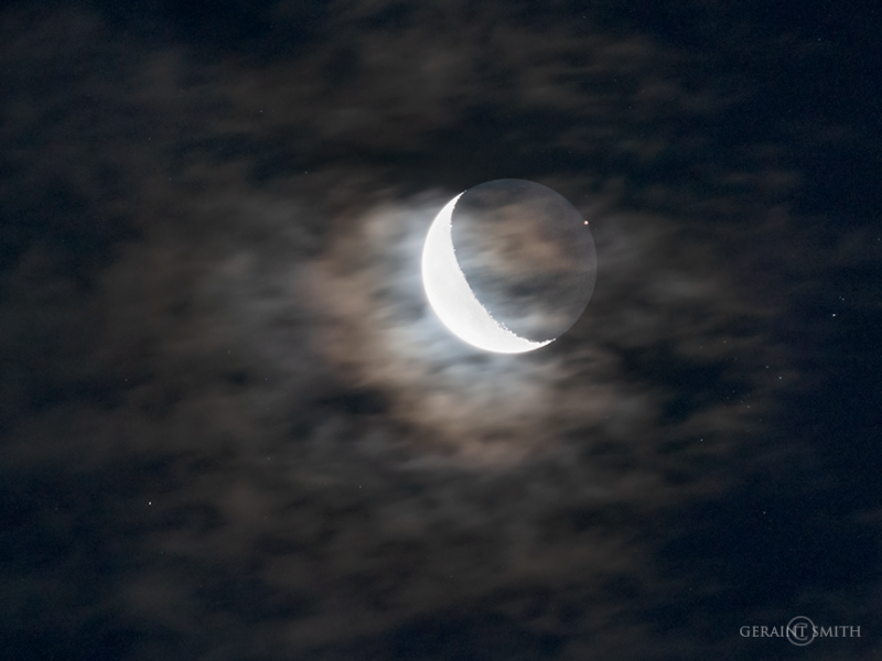 Overexposed waning moon through clouds, with bright dot of Mars nearby.