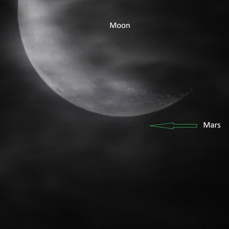 Blurry waning moon, nearly hidden by clouds, with faint Mars near the moon's lighted edge.