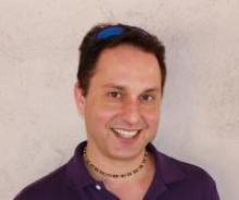 Smiling man with necklace on light-colored background.