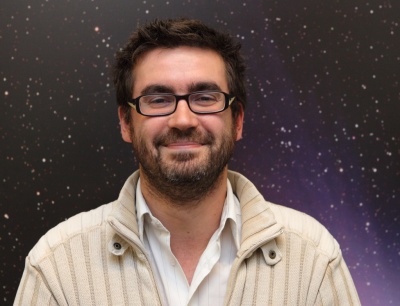 Smiling man with glasses and stars in background.