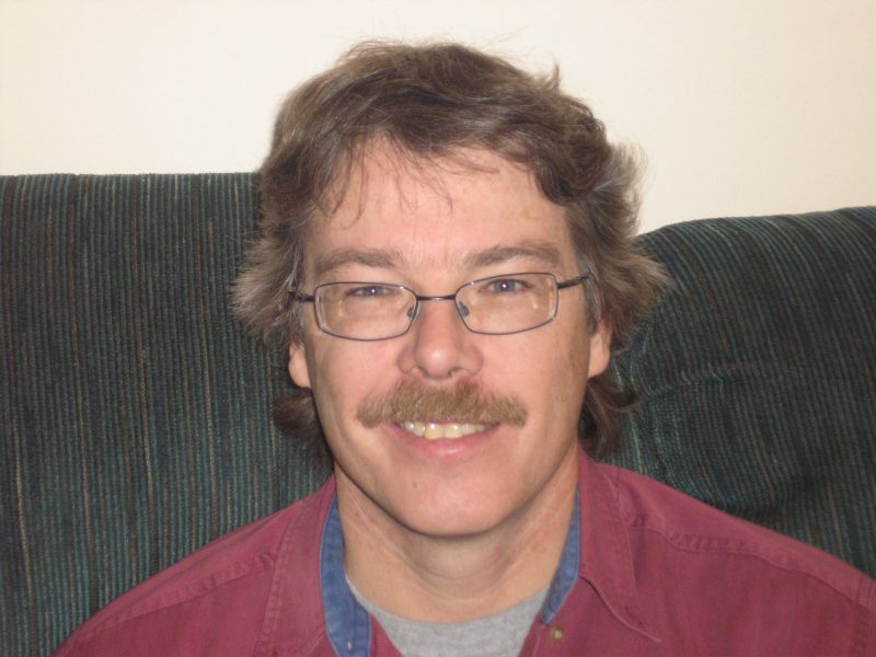 Smiling man with eyeglasses on sofa.