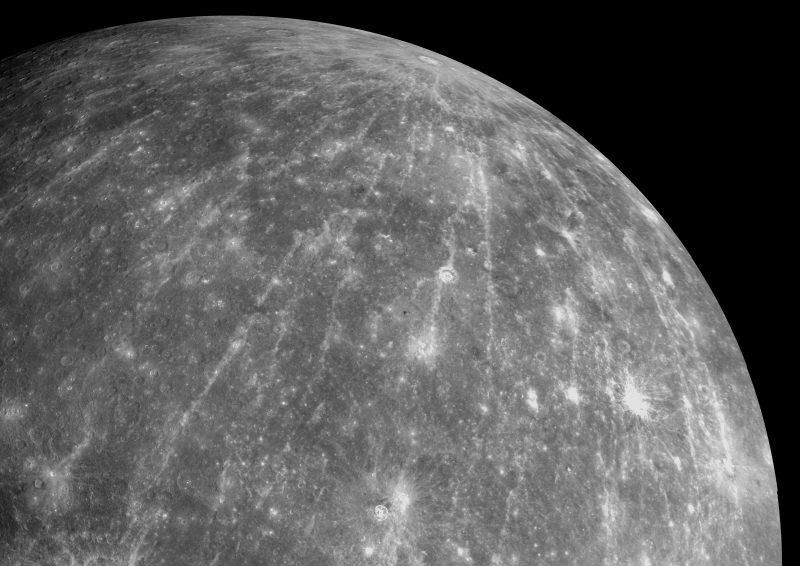 Серый шар, покрытый кратерами, на черном фоне с длинными узкими белыми полосами, расходящимися от кратера.