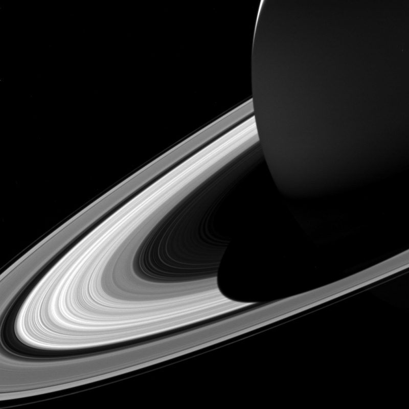 Large sphere in shadow surrounded by rings on black background.
