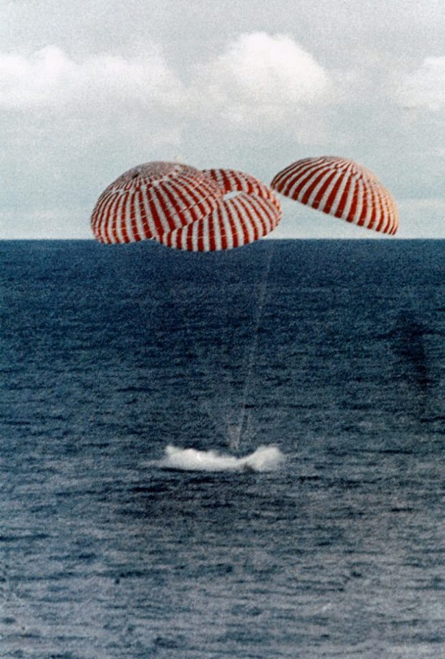 Ocean with object splashing in water, three parachutes above.