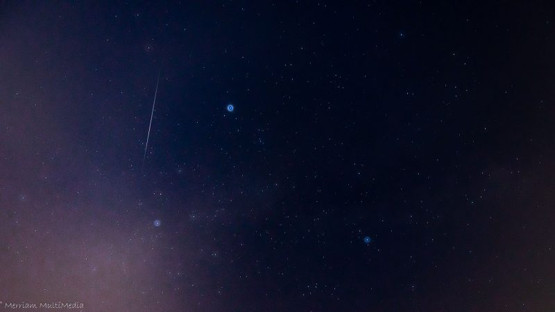 Starry sky with long thin almost vertical white streak.