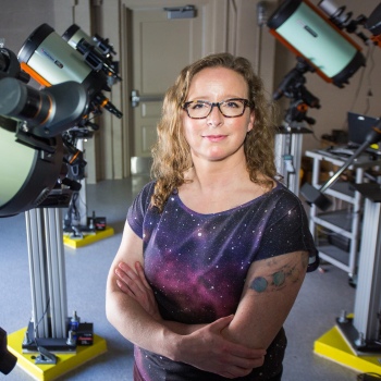 Smiling woman wearing eyeglasses and with telescopes behind her.