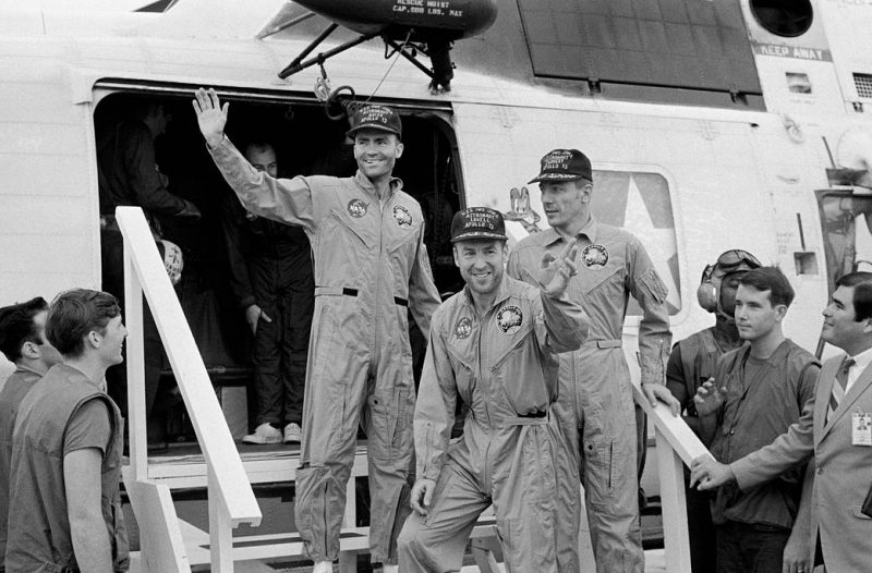 Three men in jumpsuits descending steps from a plane or helicopter.
