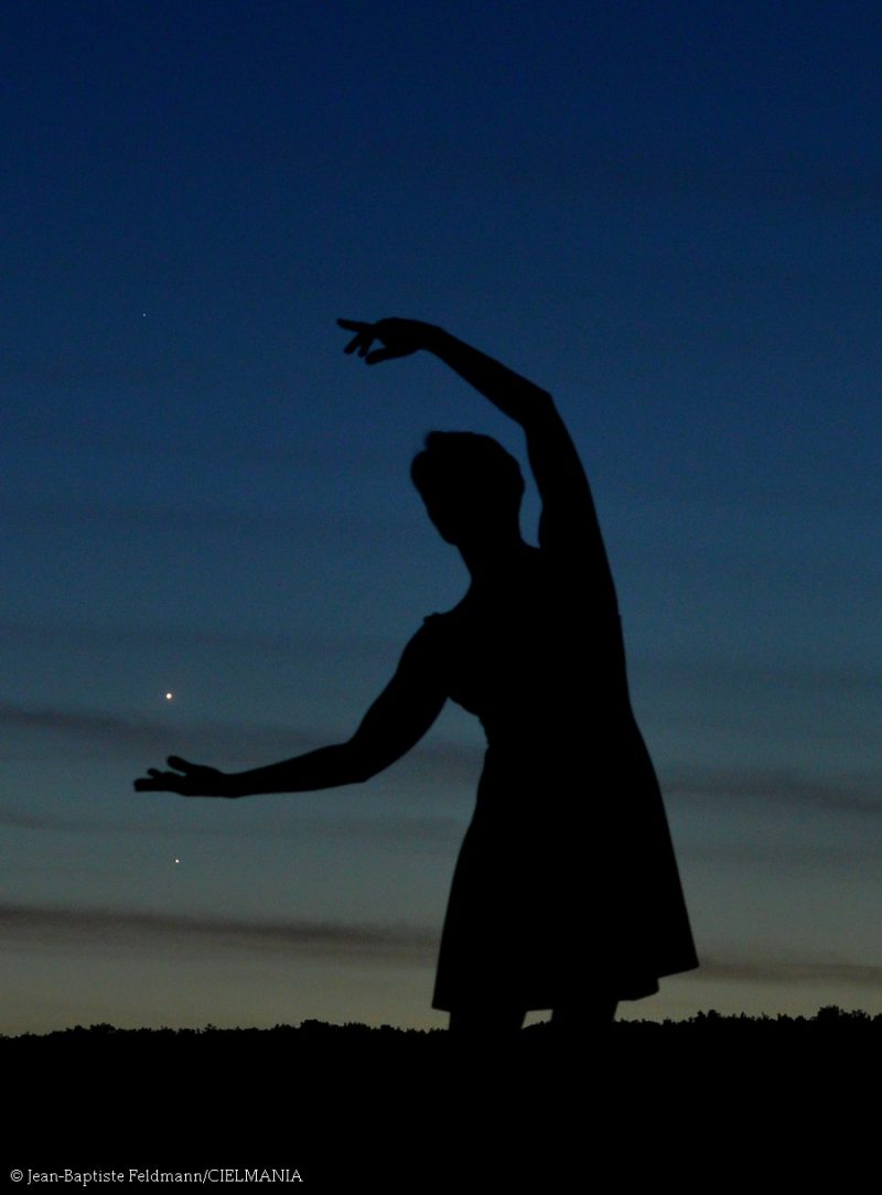 Silhouette of a ballet dancer against the sky with planets near her hands.
