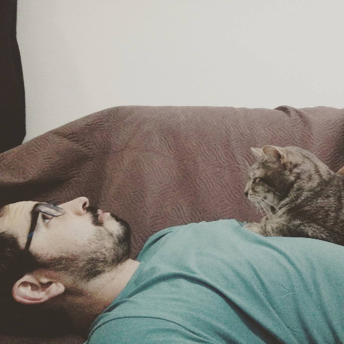 Bearded man in a green shirt lying on sofa with cat on his chest.