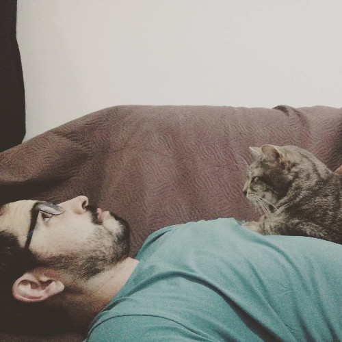 Man laying on sofa with cat on his lap.