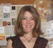 Smiling young woman with shoulder-length hair and posters in background.