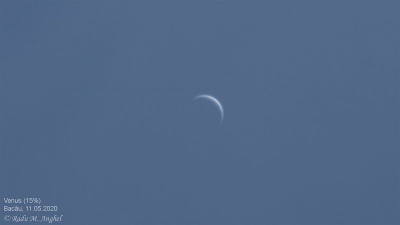 Thin crescent Venus against a blue sky.