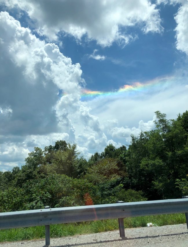 Rainbow colors on the edge of a cloud seen through a car window.