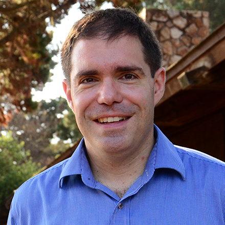 Smiling man in blue shirt with trees in background.