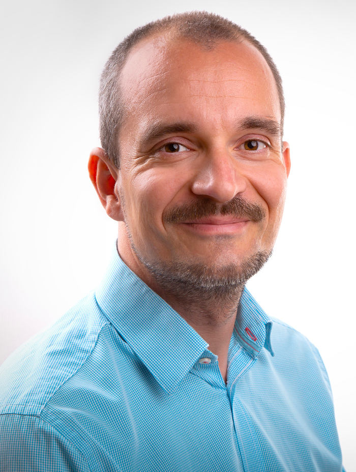 Smiling man with mustache and blue shirt on white background.
