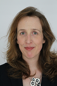 Smiling woman with long hair on light-colored background.