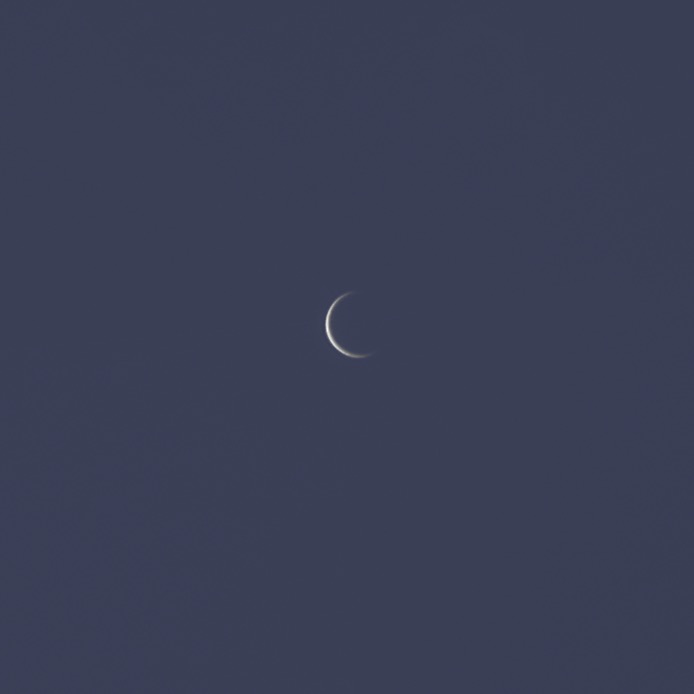A very thin crescent Venus against a blue sky.