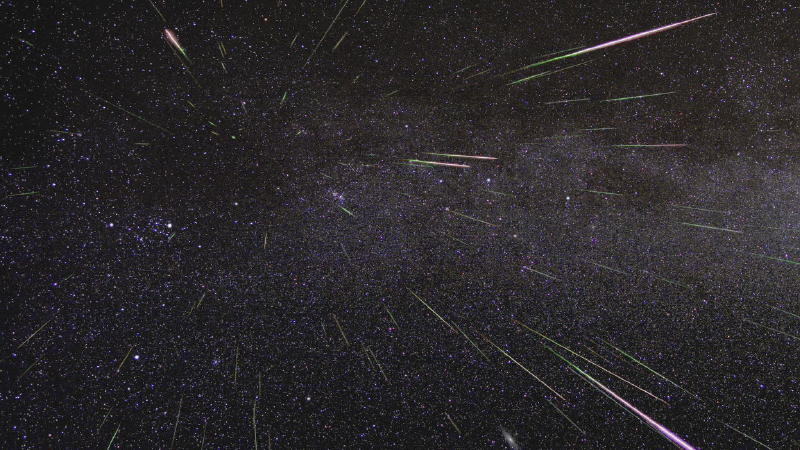 Plenty of pink and green straight lines (meteors) radiating from same place in a dark, starry sky.