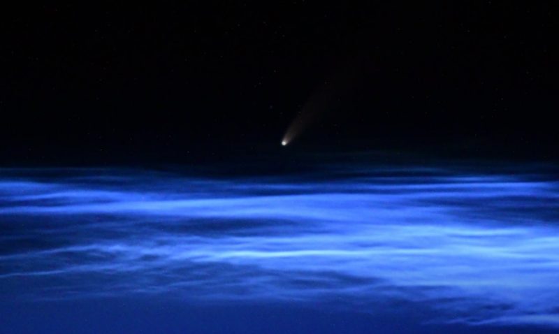Petit point lumineux avec une queue à peine visible sur des rayures bleues, ondulées et horizontales de nuages.