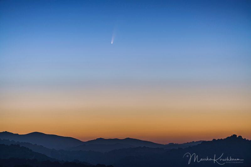 Une comète avec une queue fendue sur un ciel crépusculaire brillant sur les collines bleues.