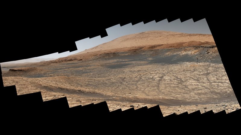 Reddish ground under light sky with hill in distance, in jagged-edged photo.