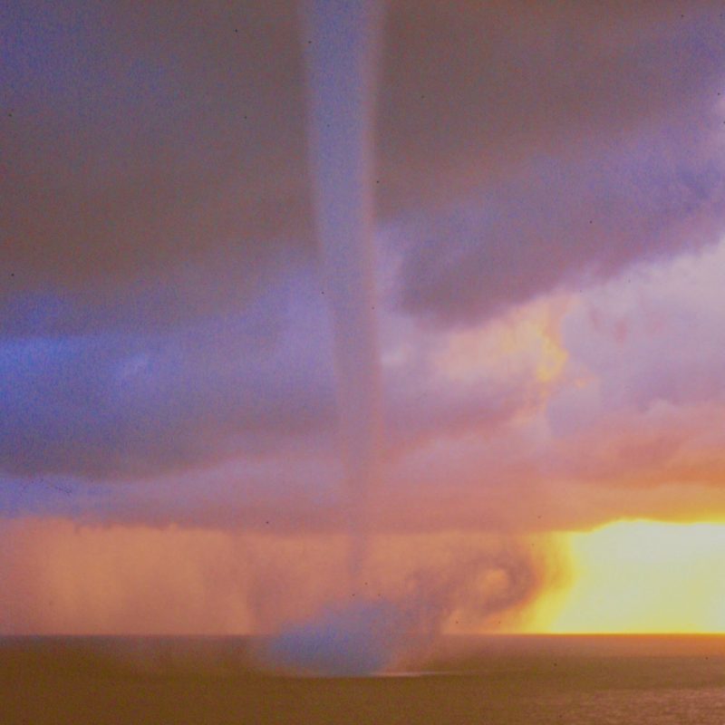 Waterspouts: Long sinuous funnel from twilight clouds to splashing ocean surface.