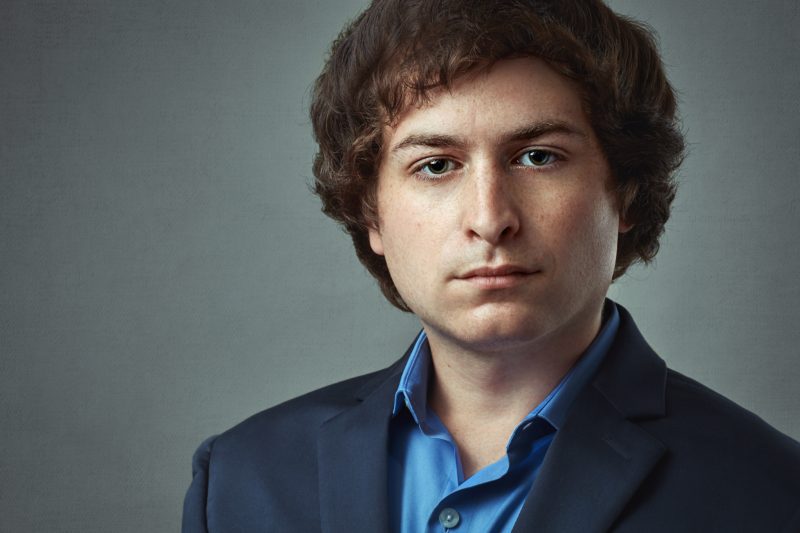 Man with curly hair with grayish background.