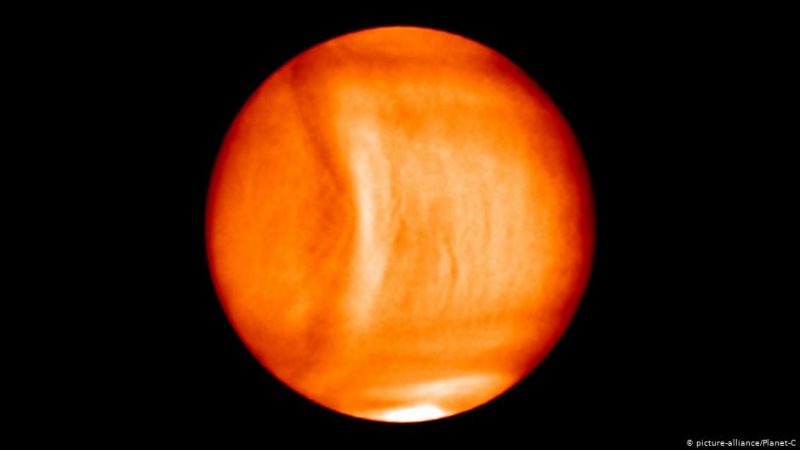 Red and ywllow false-color Venus with bow-shaped wave feature running nearly from pole to pole, on black background.
