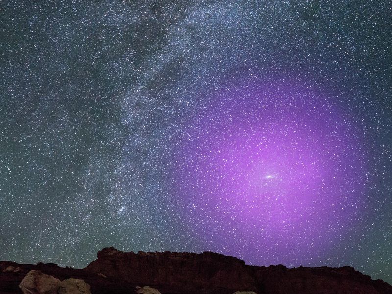 Earth's starry night sky above a mountain ridge, with a huge purple halo around the Andromeda galaxy.