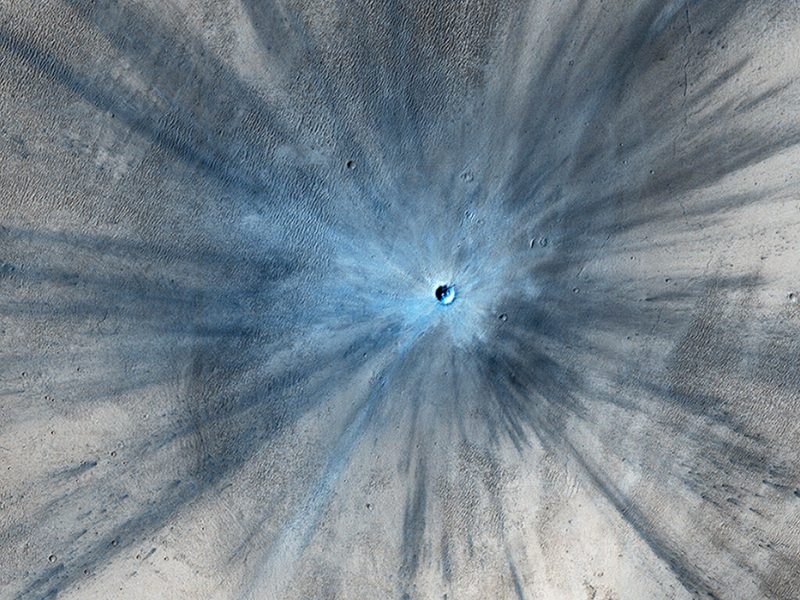 Impact crater surrounded by very long dark and shiny rays of rock debris.