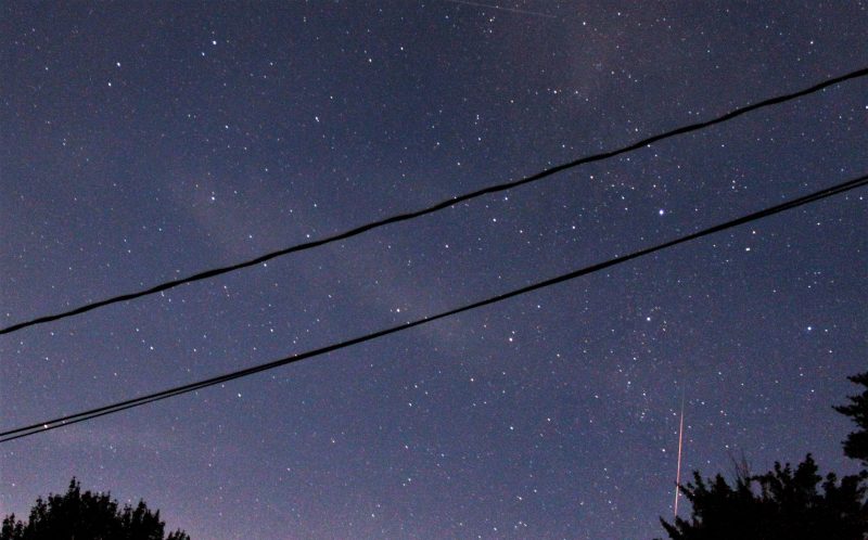 In starry sky crossed by two power lines, a thin red vertical streak.